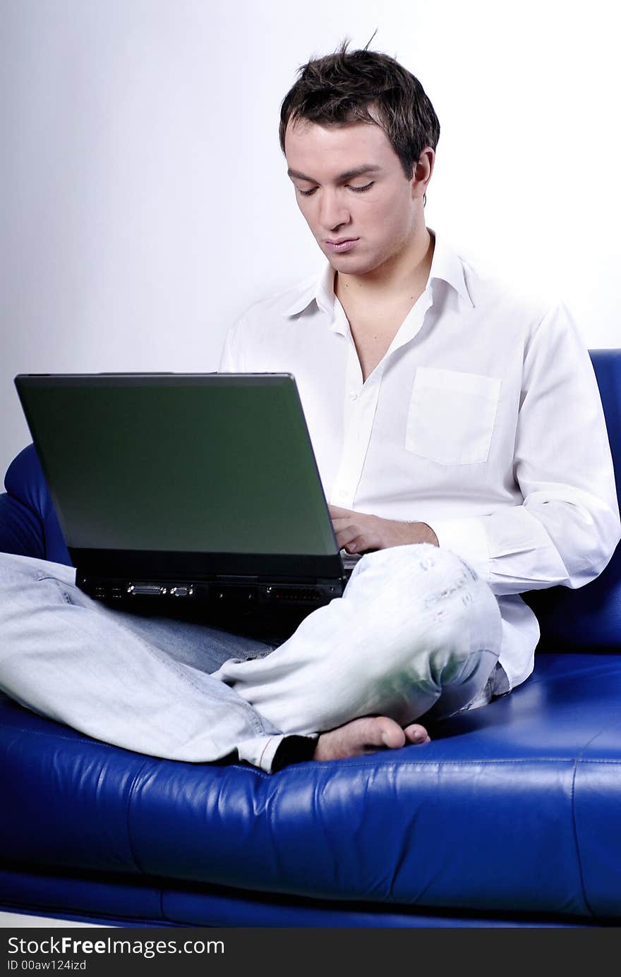 Young man comfortably sitting in a sofa using a laptop. Young man comfortably sitting in a sofa using a laptop