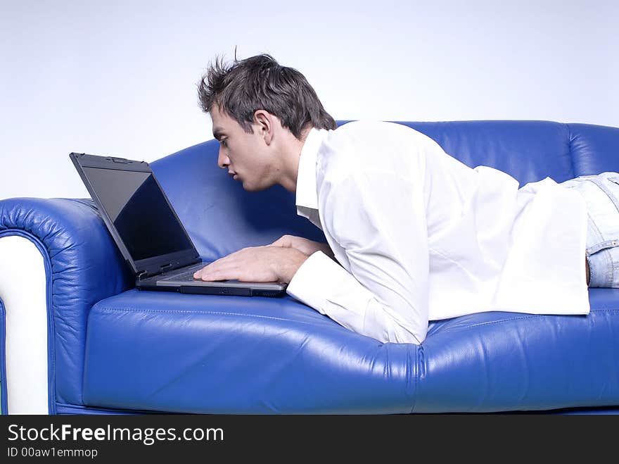 Young man comfortably sitting in a sofa using a laptop. Young man comfortably sitting in a sofa using a laptop