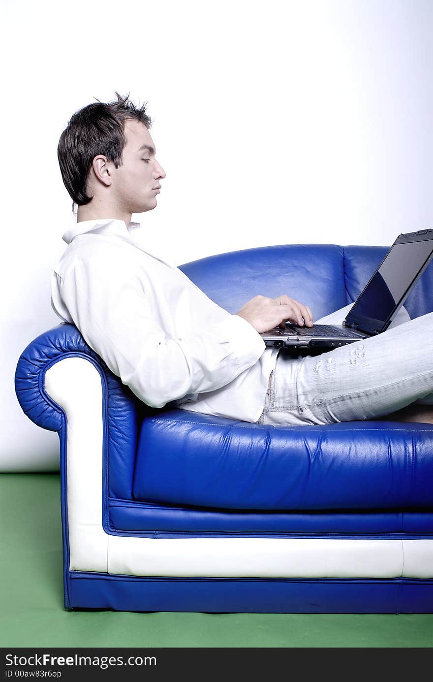 Young man comfortably sitting in a sofa using a laptop. Young man comfortably sitting in a sofa using a laptop
