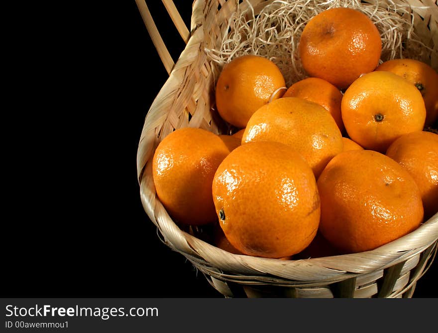 Clementines imported from Spain in a basket on a black background.  These are also knows as Satsumas and are grown in southern Louisiana.