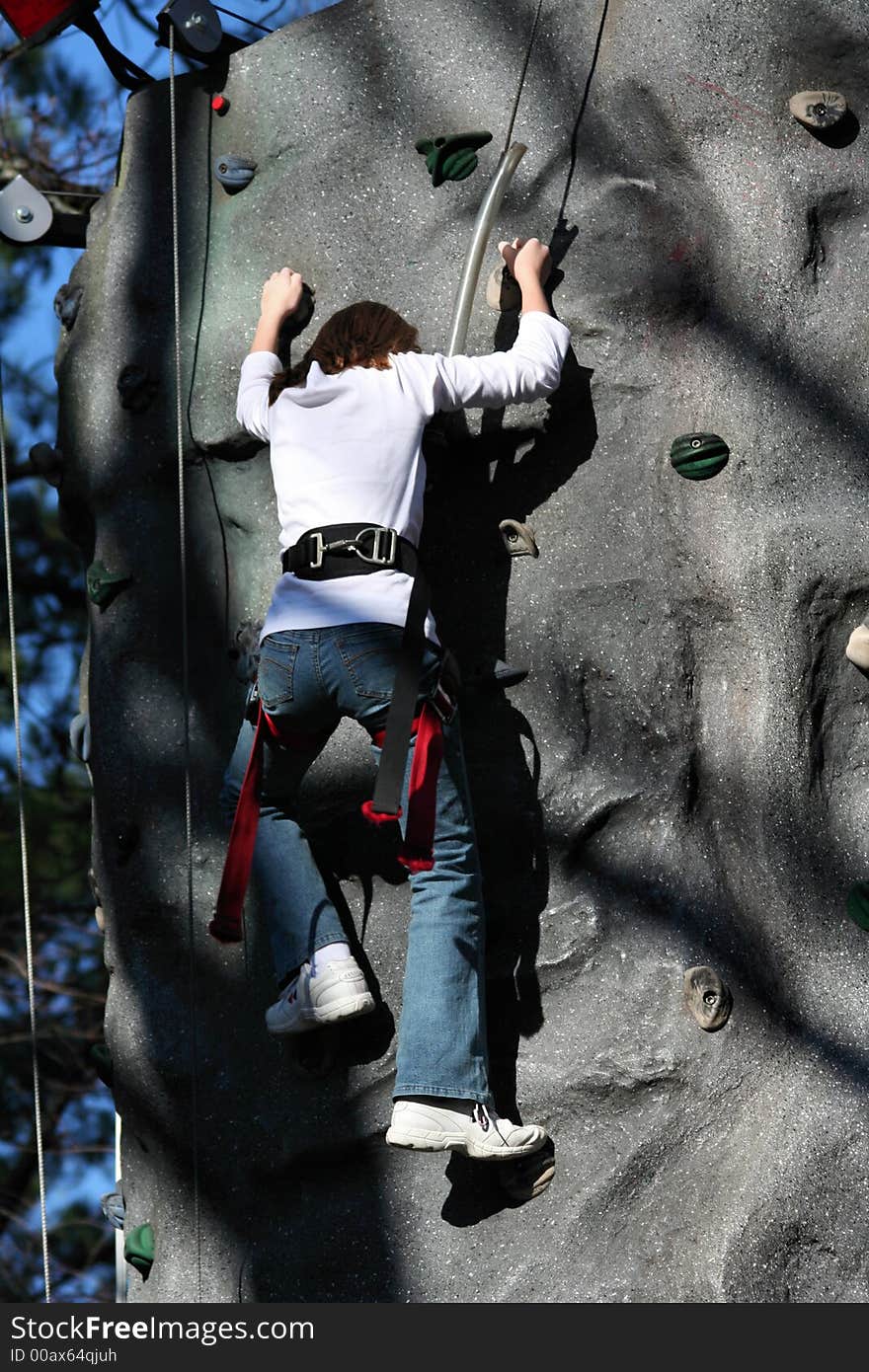 A young climber scales an artificial cliff. A young climber scales an artificial cliff.