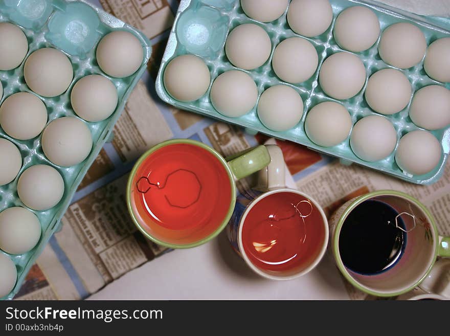 Eggs sit in an egg tray waiting to be dyed - the dye is in cups right next to the trays - unique view from directly above. Eggs sit in an egg tray waiting to be dyed - the dye is in cups right next to the trays - unique view from directly above.