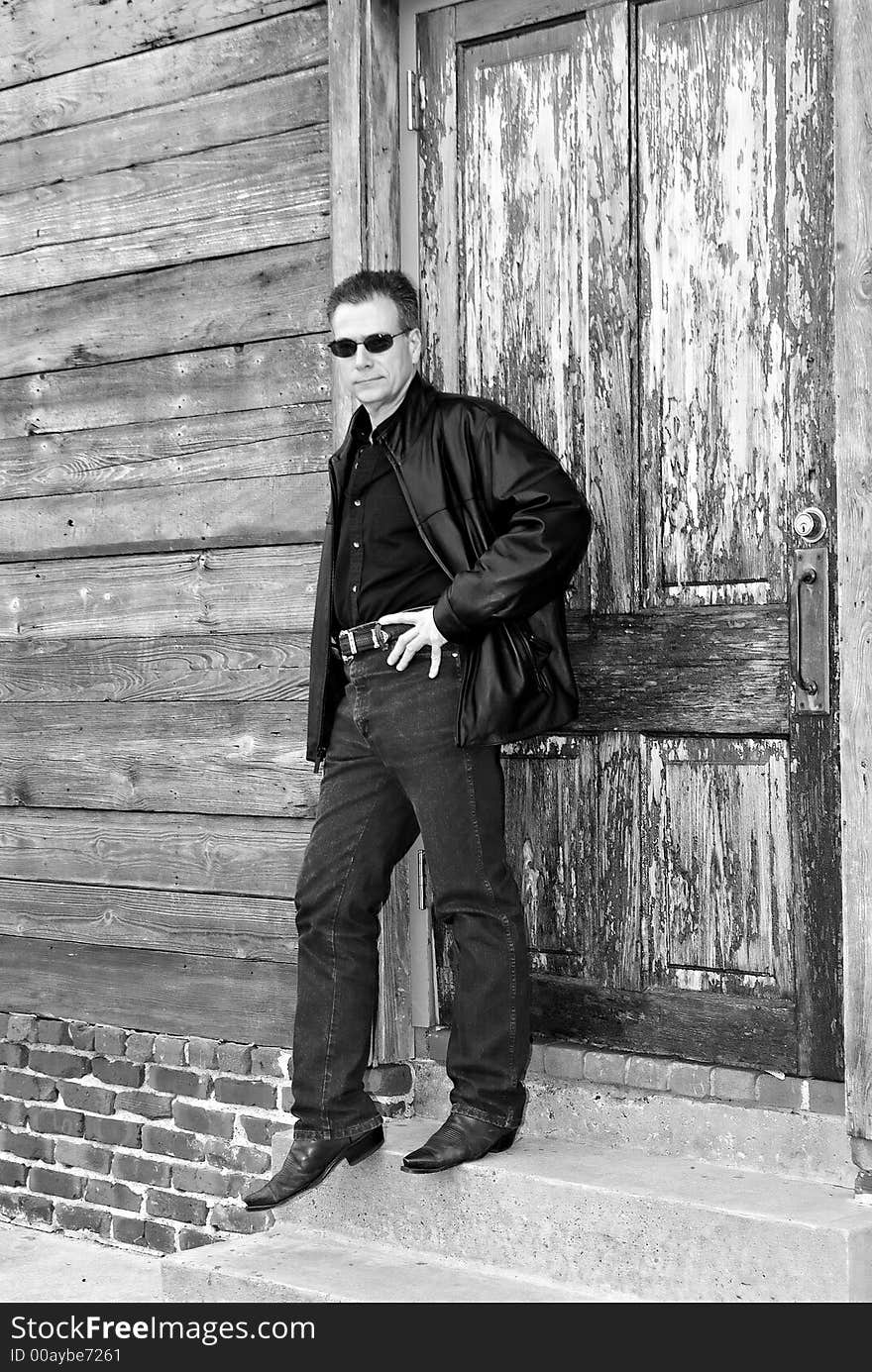 Man leaning against an old weathered door with a cool, casual demeanor. Man leaning against an old weathered door with a cool, casual demeanor.