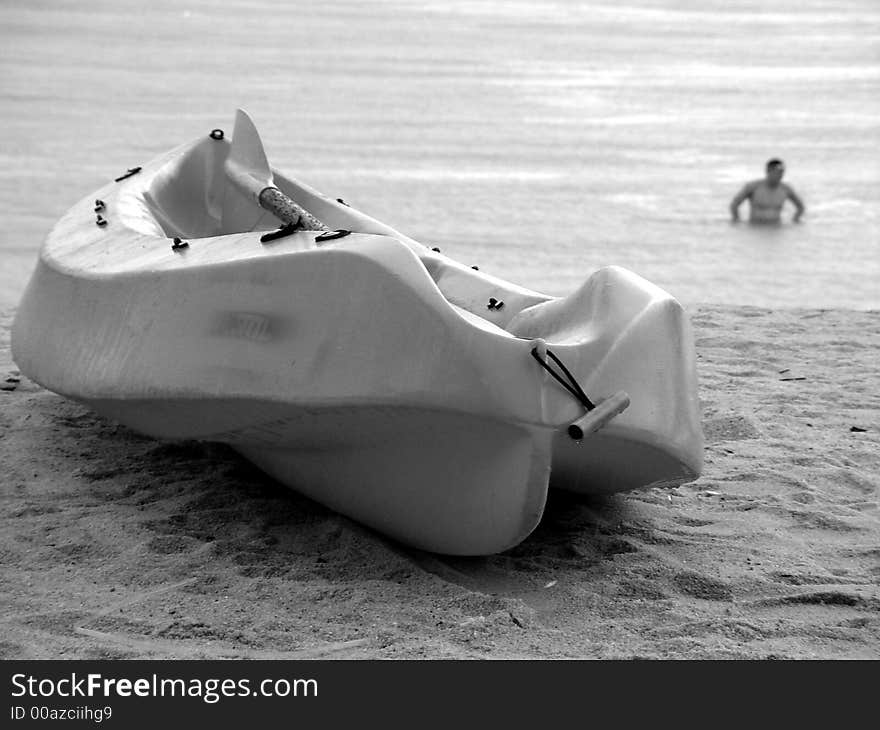 A rescue canoe or kayak beach on the sandy shore, in the background is a person in the water.Location is sentosa tanjong beach in singapore. monochrome image. A rescue canoe or kayak beach on the sandy shore, in the background is a person in the water.Location is sentosa tanjong beach in singapore. monochrome image.