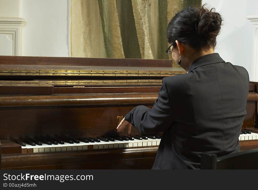 Portrait of a female piano teacher looking downward as she plays piano. Shot from back view. Portrait of a female piano teacher looking downward as she plays piano. Shot from back view.