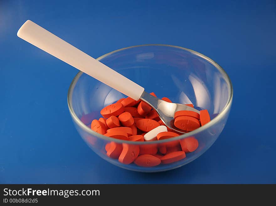 A bowl and spoon with a serving of red pills with one odd white one sit on a blue background. A bowl and spoon with a serving of red pills with one odd white one sit on a blue background.