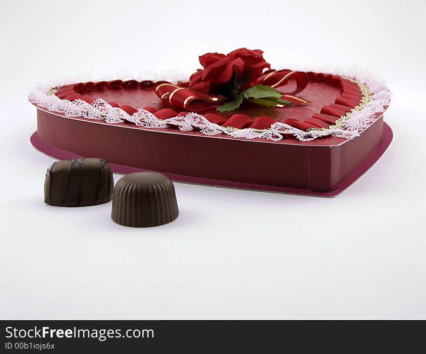 Photo of a box of valentine chocolates in a heart shape with two chocolates outside the box.