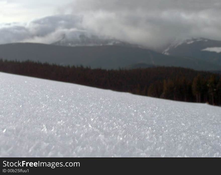 Snow-covered surface of the mountainside (and not in focus mountain and clouds behind). Snow-covered surface of the mountainside (and not in focus mountain and clouds behind)