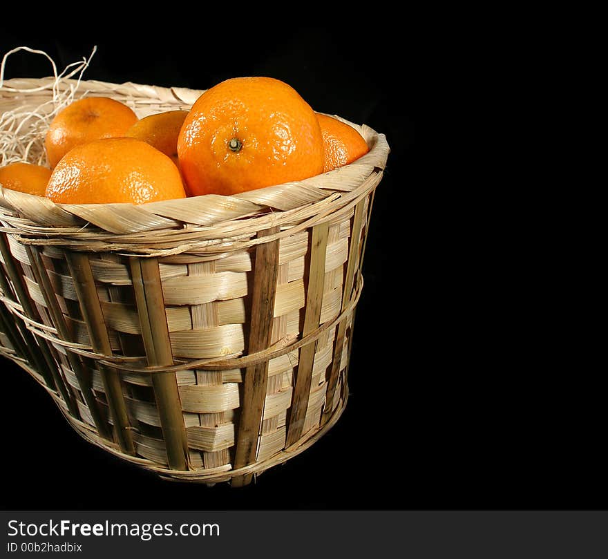 Clementines imported from Spain in a basket on a black background.  These are also knows as Satsumas and are grown in southern Louisiana.