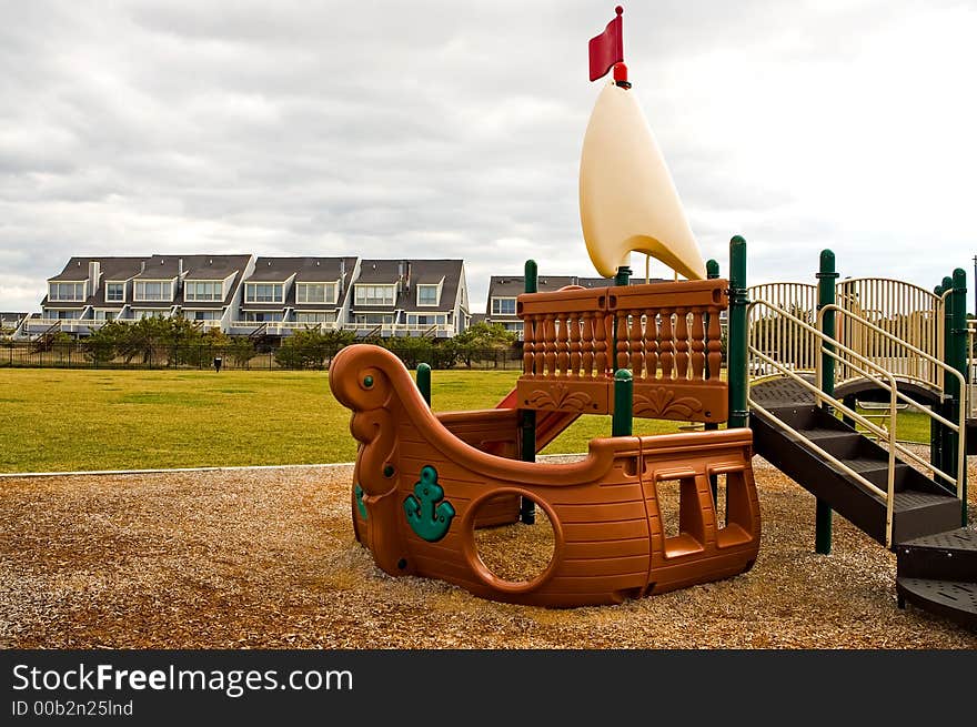 A big, plastic pirate ship makes up part of a outdoor playground for children to climb on and play with.