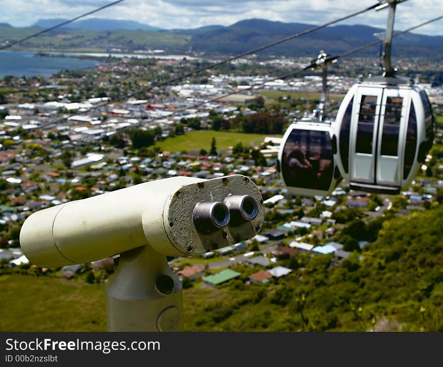 Tourist telescope with gondola cars overlooking the city, lake and distant mountains with emphasis on the telescope by using a shallow DOF. Tourist telescope with gondola cars overlooking the city, lake and distant mountains with emphasis on the telescope by using a shallow DOF