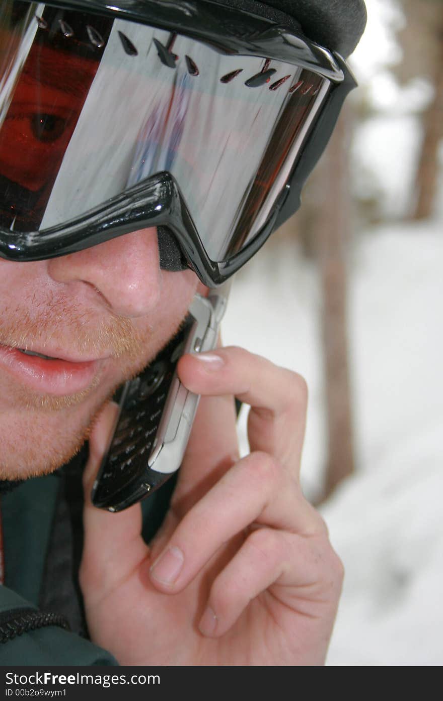 A man uses his cell phone while enjoying the outdoors skiing . A man uses his cell phone while enjoying the outdoors skiing