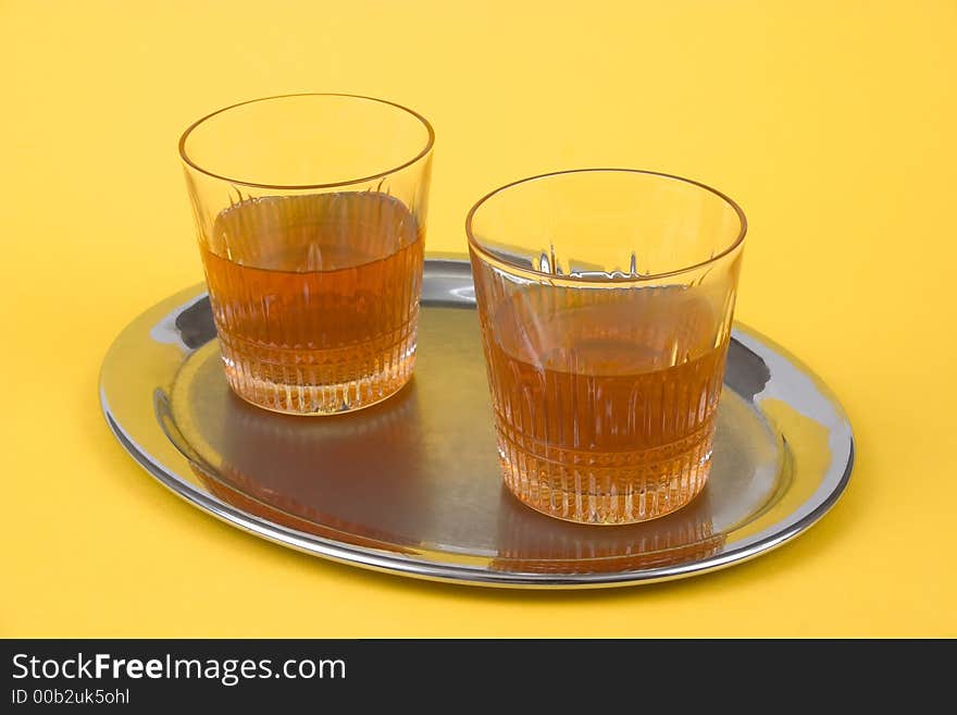 Two glasses with whiskey standing on a silver tray on yellow background