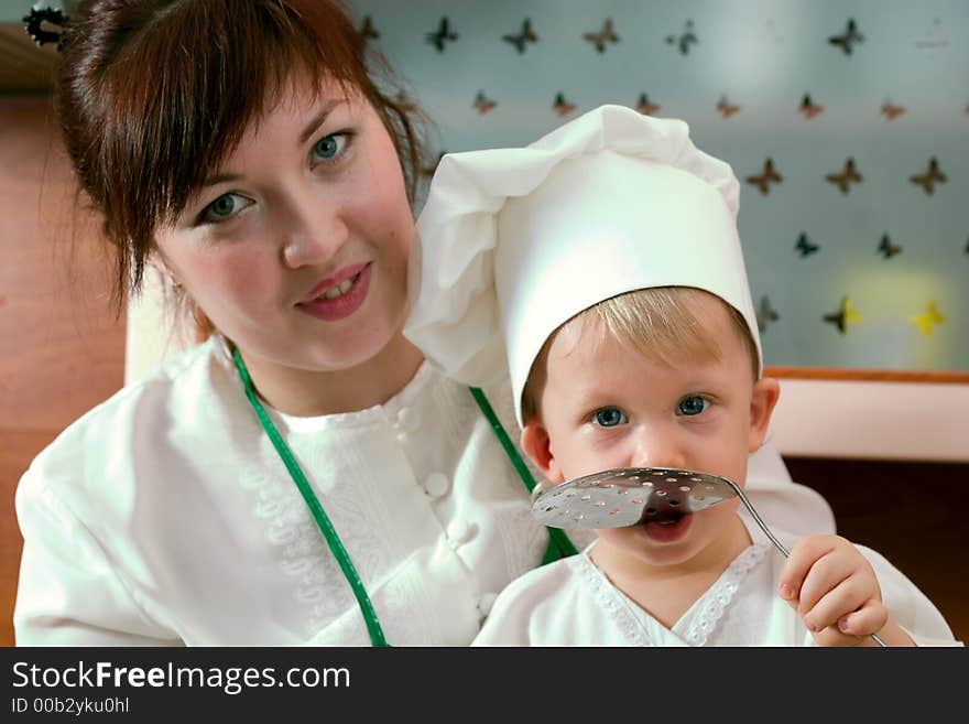 Laughing mother and her little son in cook costume at the kitchen. Laughing mother and her little son in cook costume at the kitchen