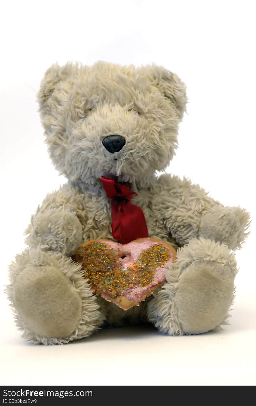 Toy bear with ginger heart cookie sitting against white background