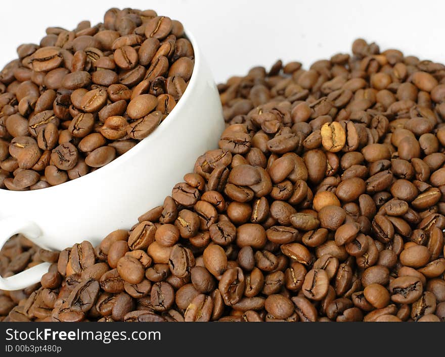 A cup of coffee full with coffee beans in the middle of a heap of coffee beans stacks. A cup of coffee full with coffee beans in the middle of a heap of coffee beans stacks.