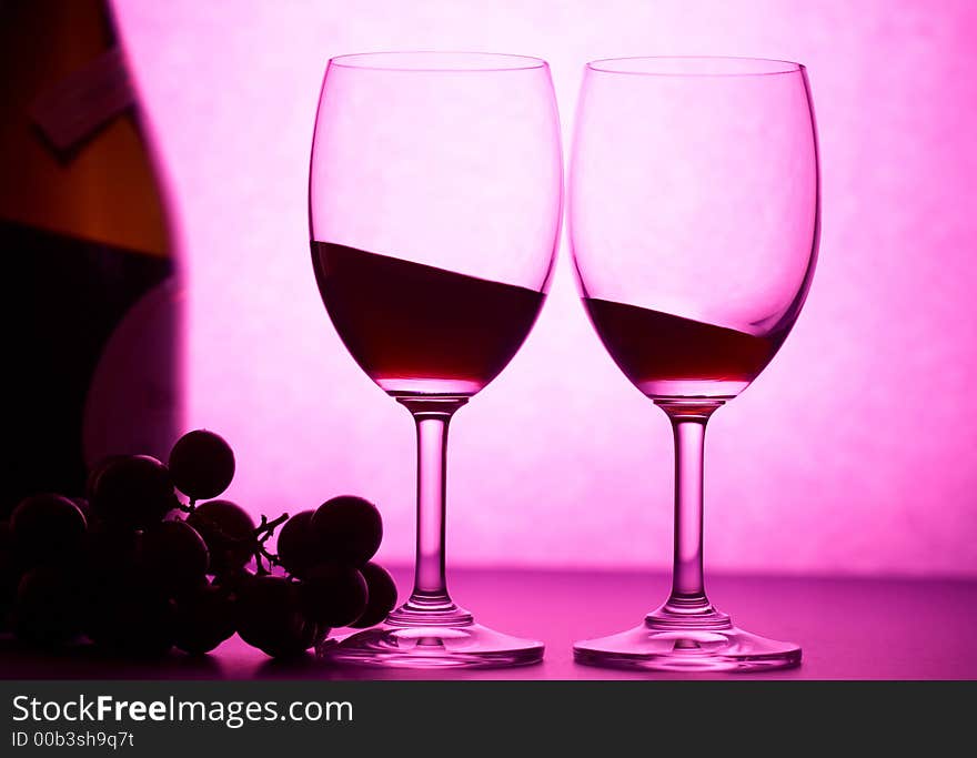 Two wineglasses with some grape in pink light. Two wineglasses with some grape in pink light