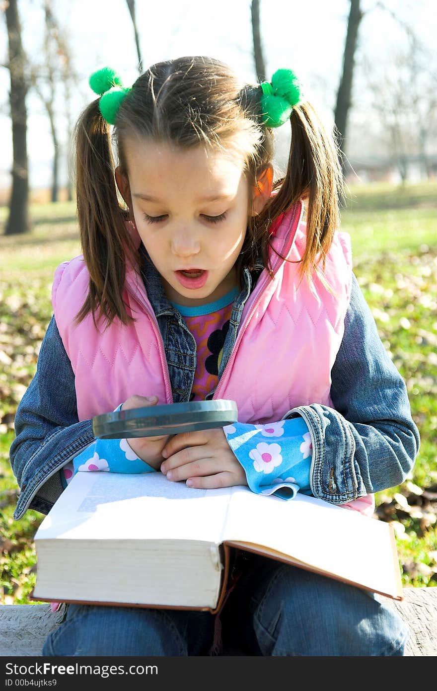 Little pretty child reading the book in the park