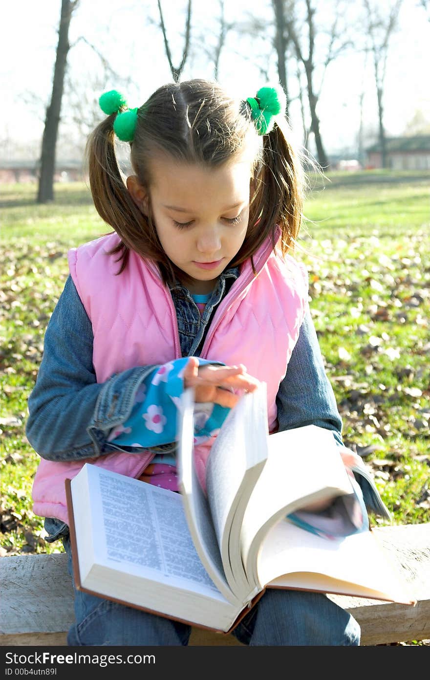 Little pretty child reading the book in the park