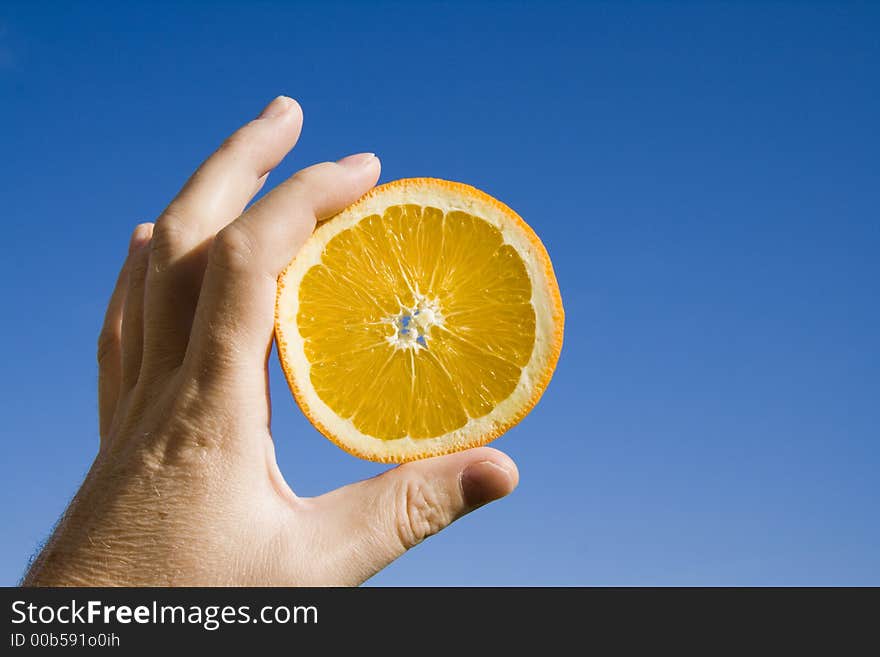 Hand holding an orange slice against clear blue sky background. Hand holding an orange slice against clear blue sky background