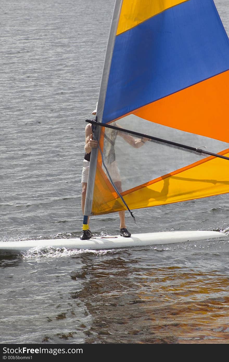 Elderly senior citizen surfing on a windsurfer board wearing a life jacket and hat. Elderly senior citizen surfing on a windsurfer board wearing a life jacket and hat