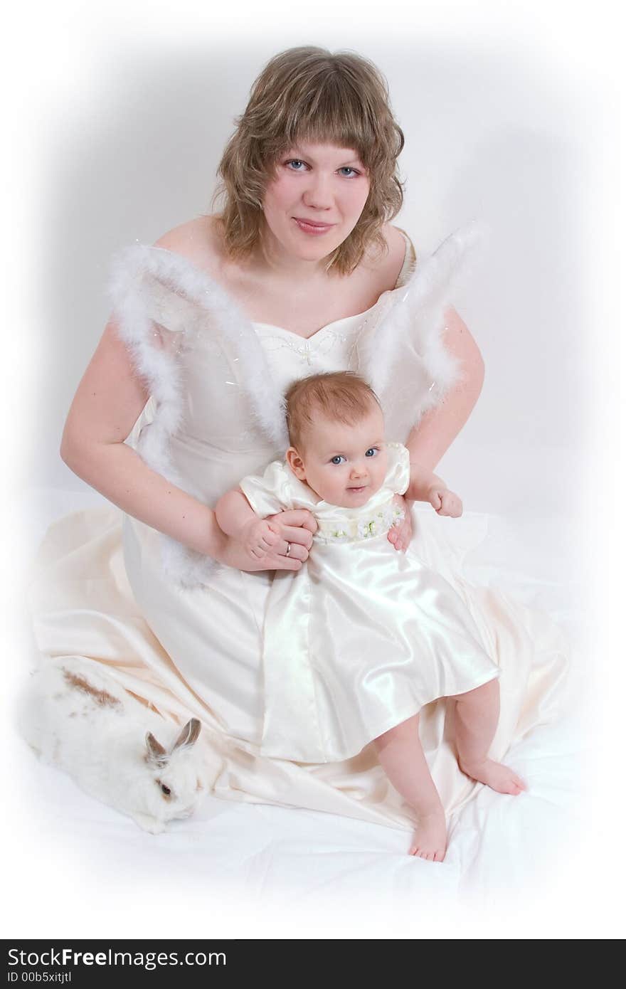 Mother and baby with rabbit are posing on white and looking into the camera