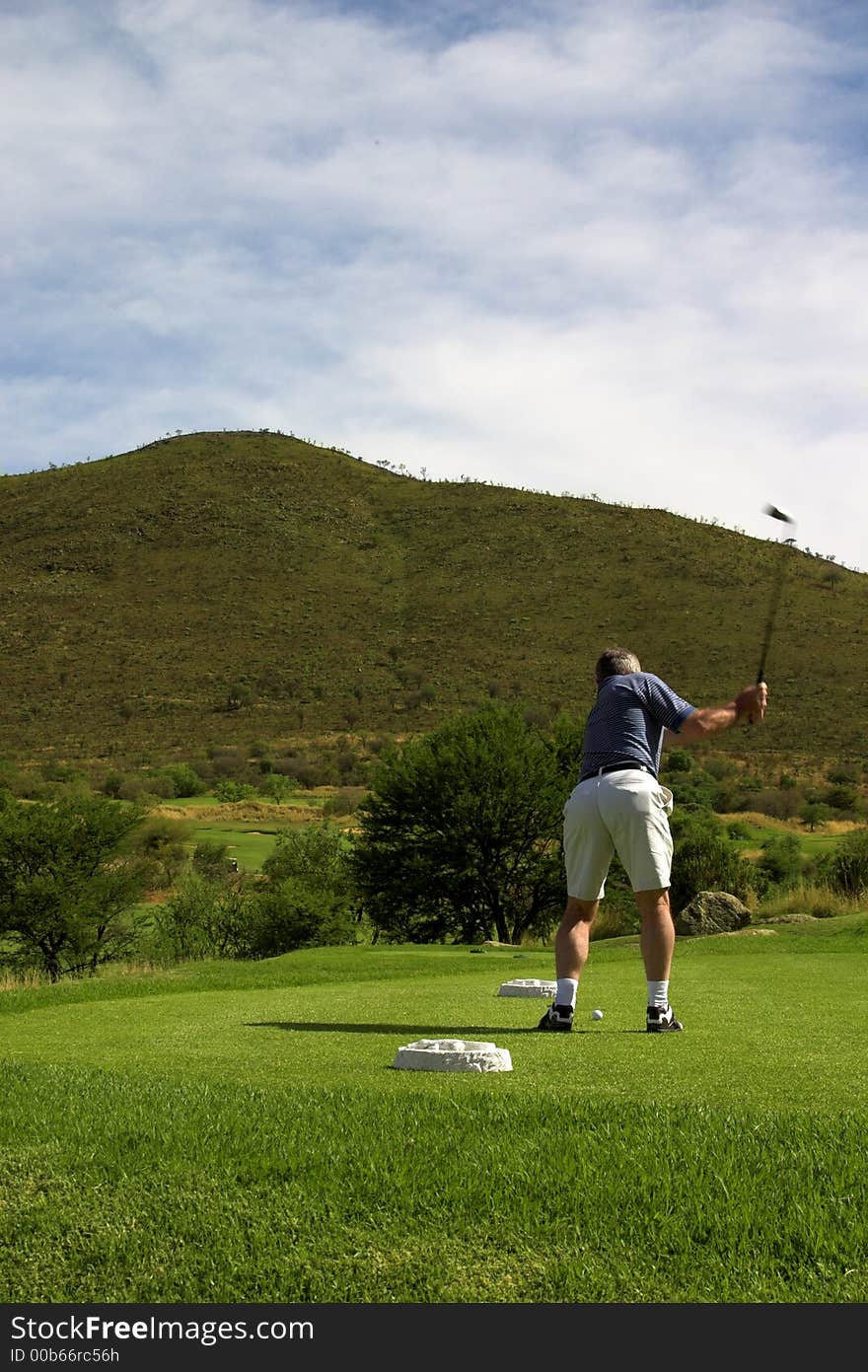 Golfer hitting a ball on the tee box. Club is in motion. Golfer hitting a ball on the tee box. Club is in motion.