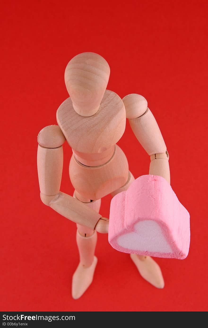 Wood manikin closeup holding a pink and white heart shaped marshmallow Valentine candy. Wood manikin closeup holding a pink and white heart shaped marshmallow Valentine candy.