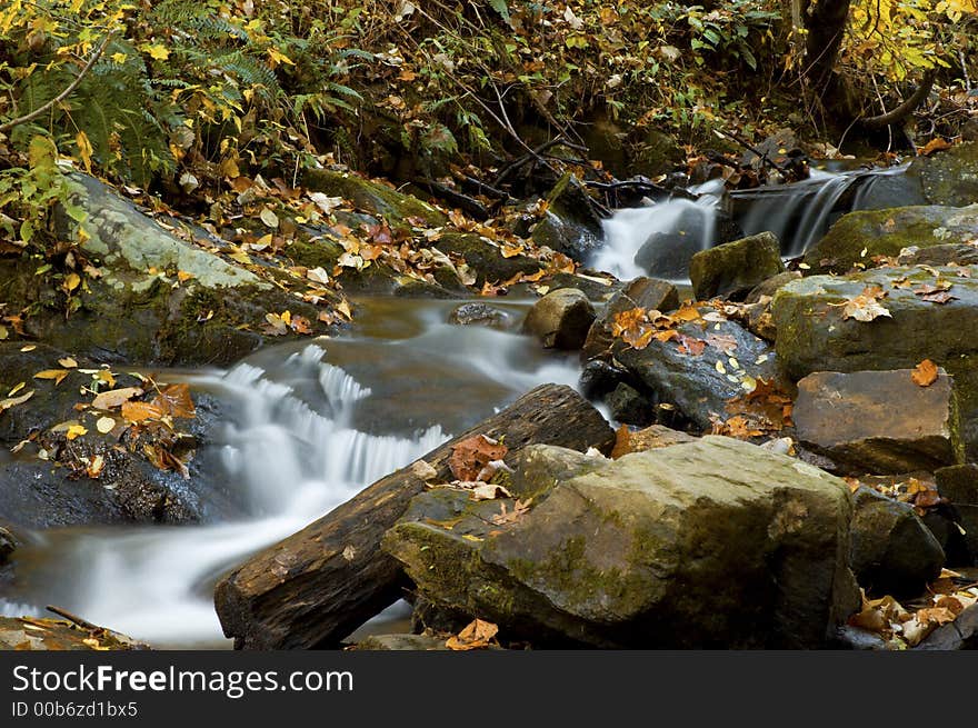 Small waterfall during the fall season with autumn color leaves and rocks framing the water. This photo was taken in the Georgian mountains. Small waterfall during the fall season with autumn color leaves and rocks framing the water. This photo was taken in the Georgian mountains.