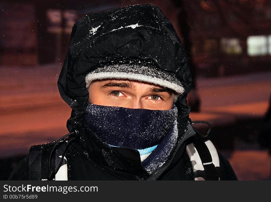 Portrait of the young guy, wrapped up in a bright scarf, which walks on city during a snowfall. Portrait of the young guy, wrapped up in a bright scarf, which walks on city during a snowfall