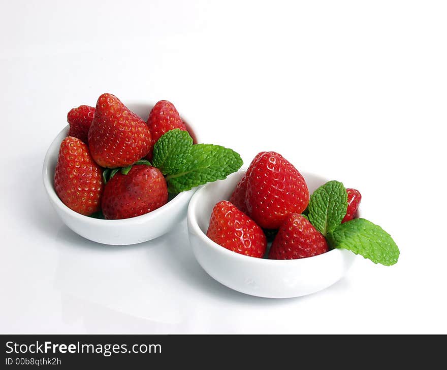 Two strawberry little bowls with mint on white background