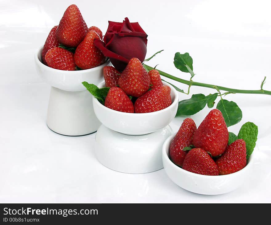 Some strawberry little bowls with mint on white background and one valentine rose