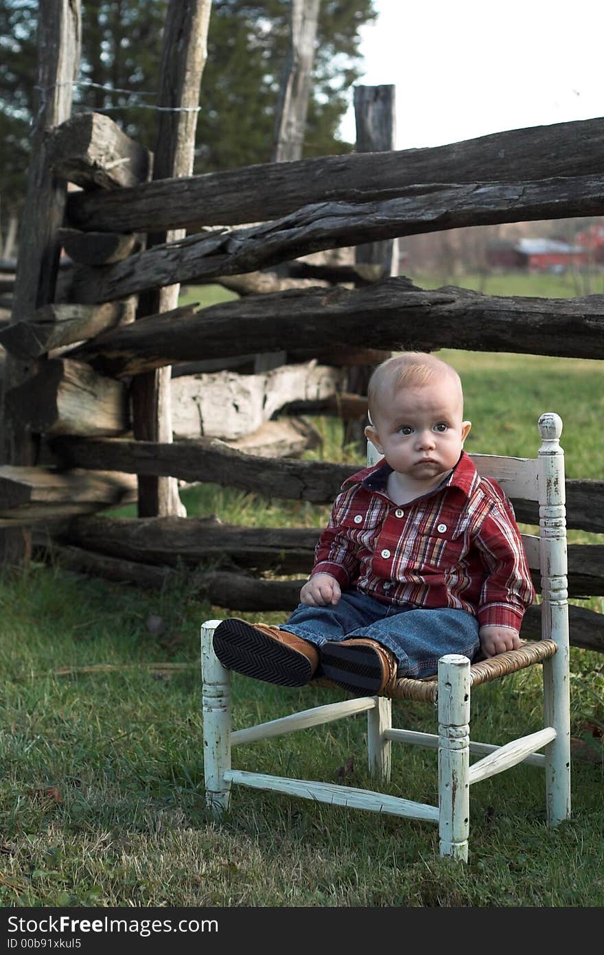 Image of baby boy sitting on a chair in front of a fence. Image of baby boy sitting on a chair in front of a fence