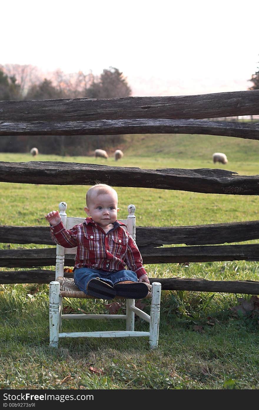 Image of baby boy sitting on a chair in front of a fence. Image of baby boy sitting on a chair in front of a fence