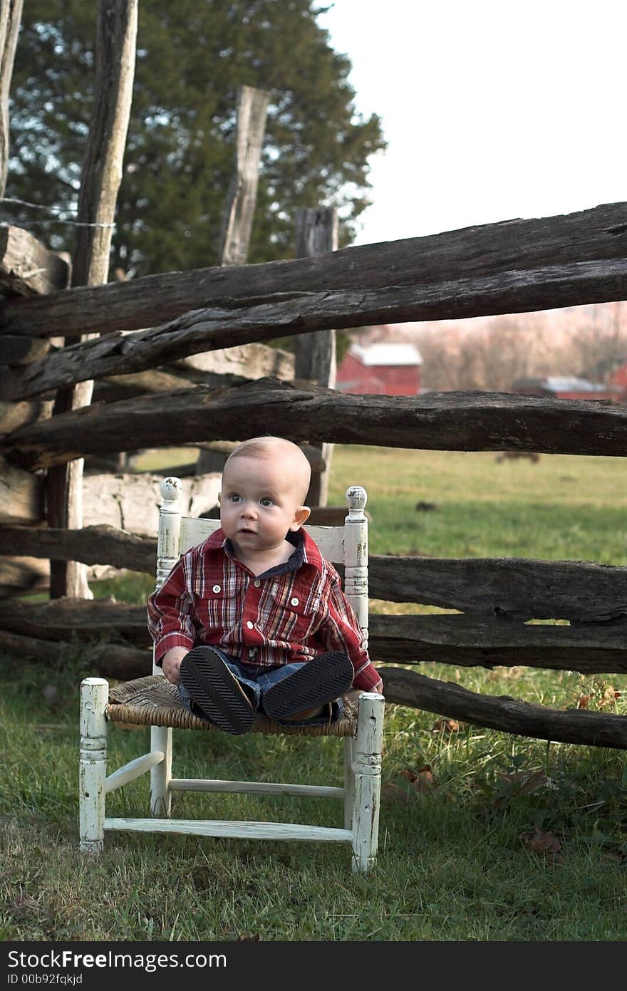 Image of baby boy sitting on a chair in front of a fence. Image of baby boy sitting on a chair in front of a fence