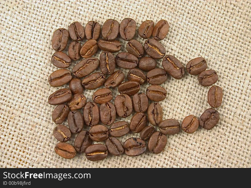 Mug made of coffee beans lying on flax background