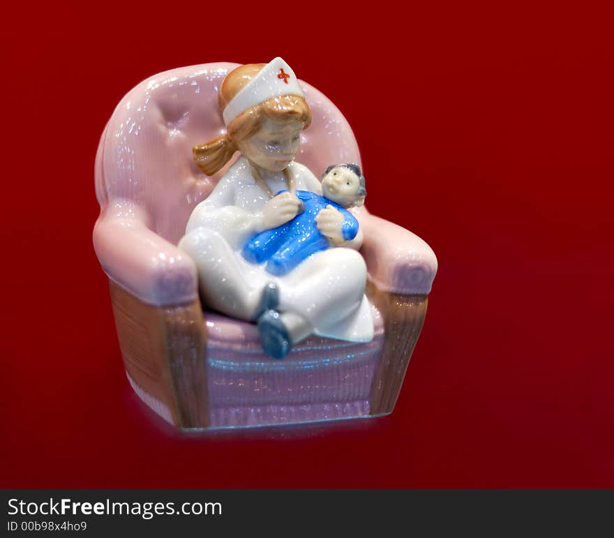 Young nurse with a baby decorative figurine isolated with clipping path on dark red background. Young nurse with a baby decorative figurine isolated with clipping path on dark red background