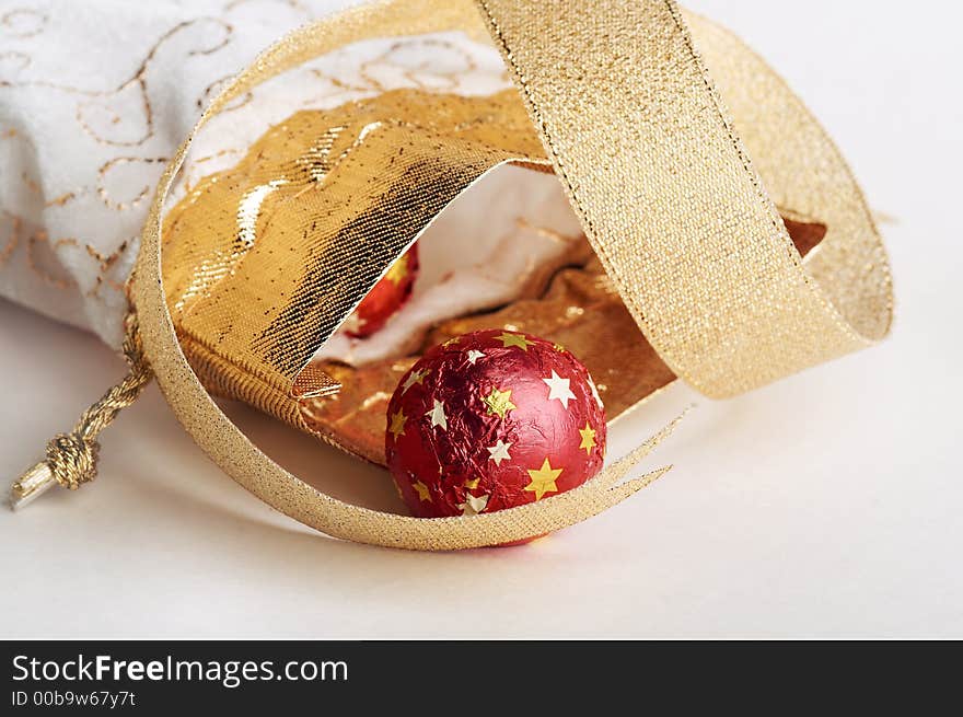 Chocolate candy in red metallic paper with stars lay near white & golden bag for gifts & golden strip on white background. Chocolate candy in red metallic paper with stars lay near white & golden bag for gifts & golden strip on white background.