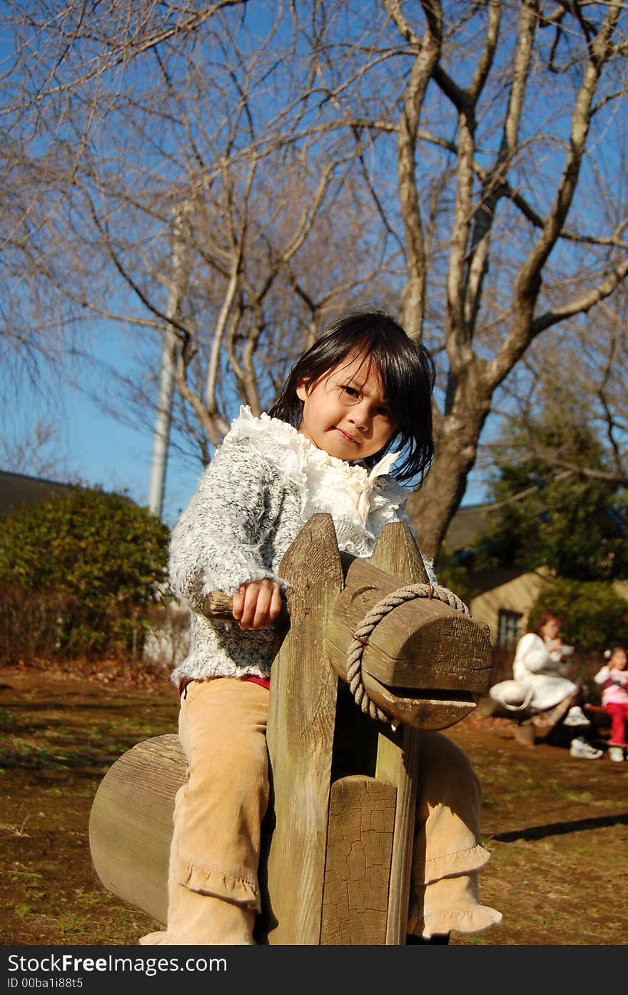 A young asian girl rides wooden horse at park. A young asian girl rides wooden horse at park.