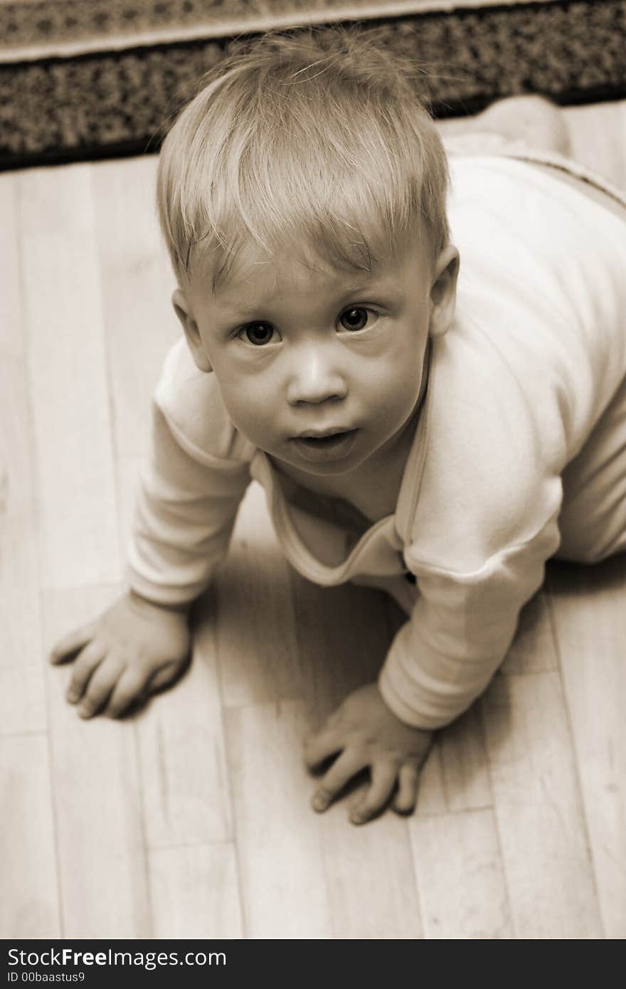 Cute little boy on the warm wooden floor looking into camera. Sepia