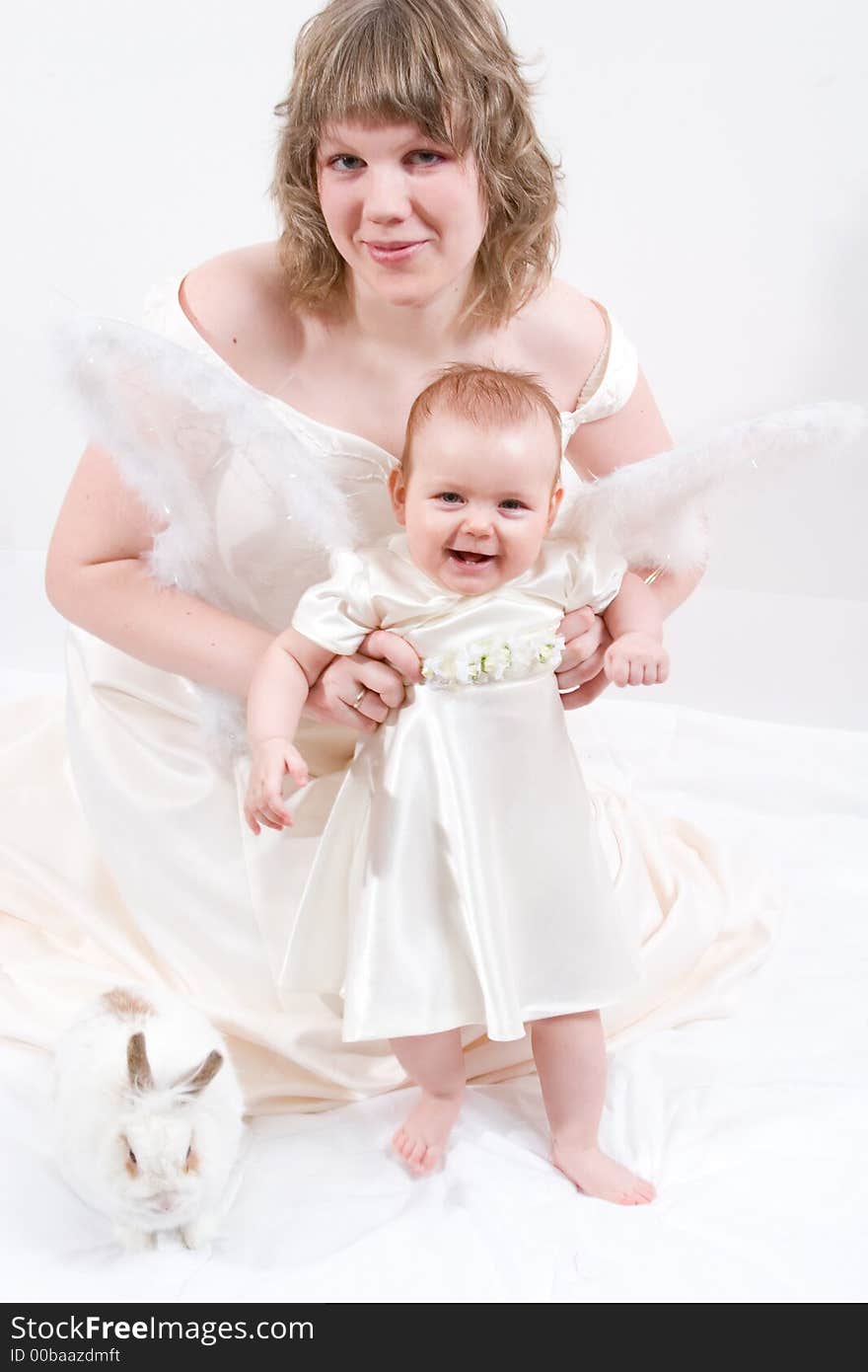 Mother and baby with rabbit are posing on white and looking into the camera