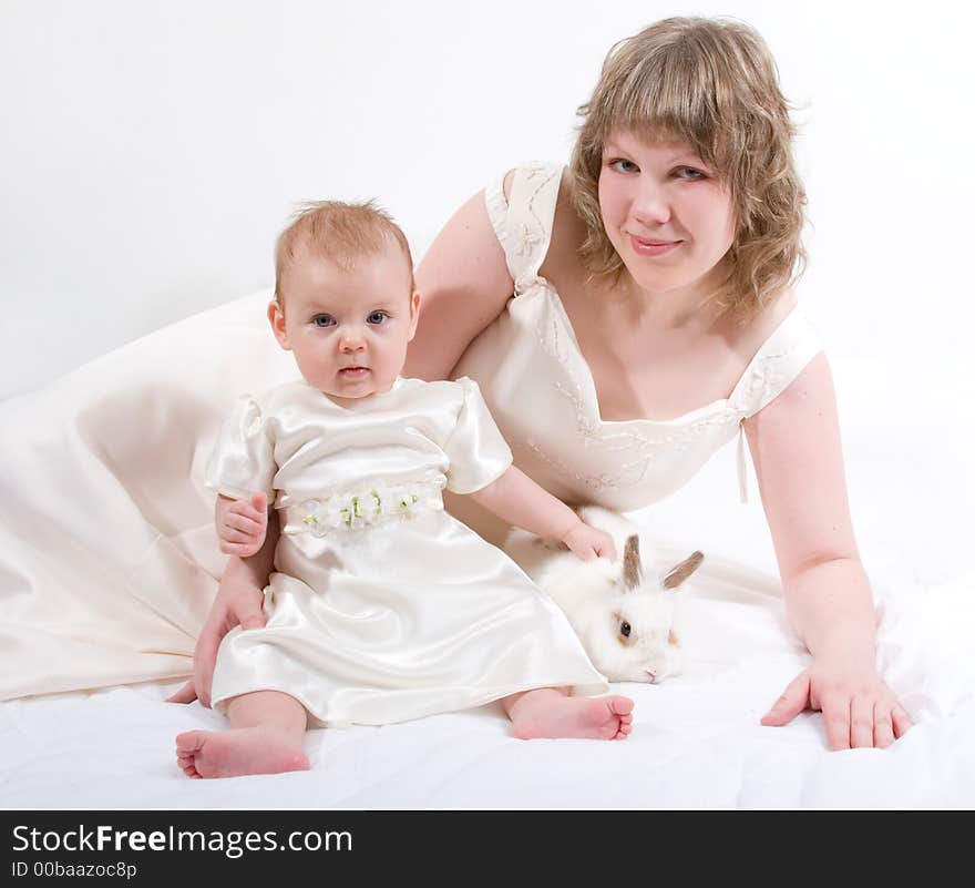 Mother and baby with rabbit are posing on white and looking into the camera