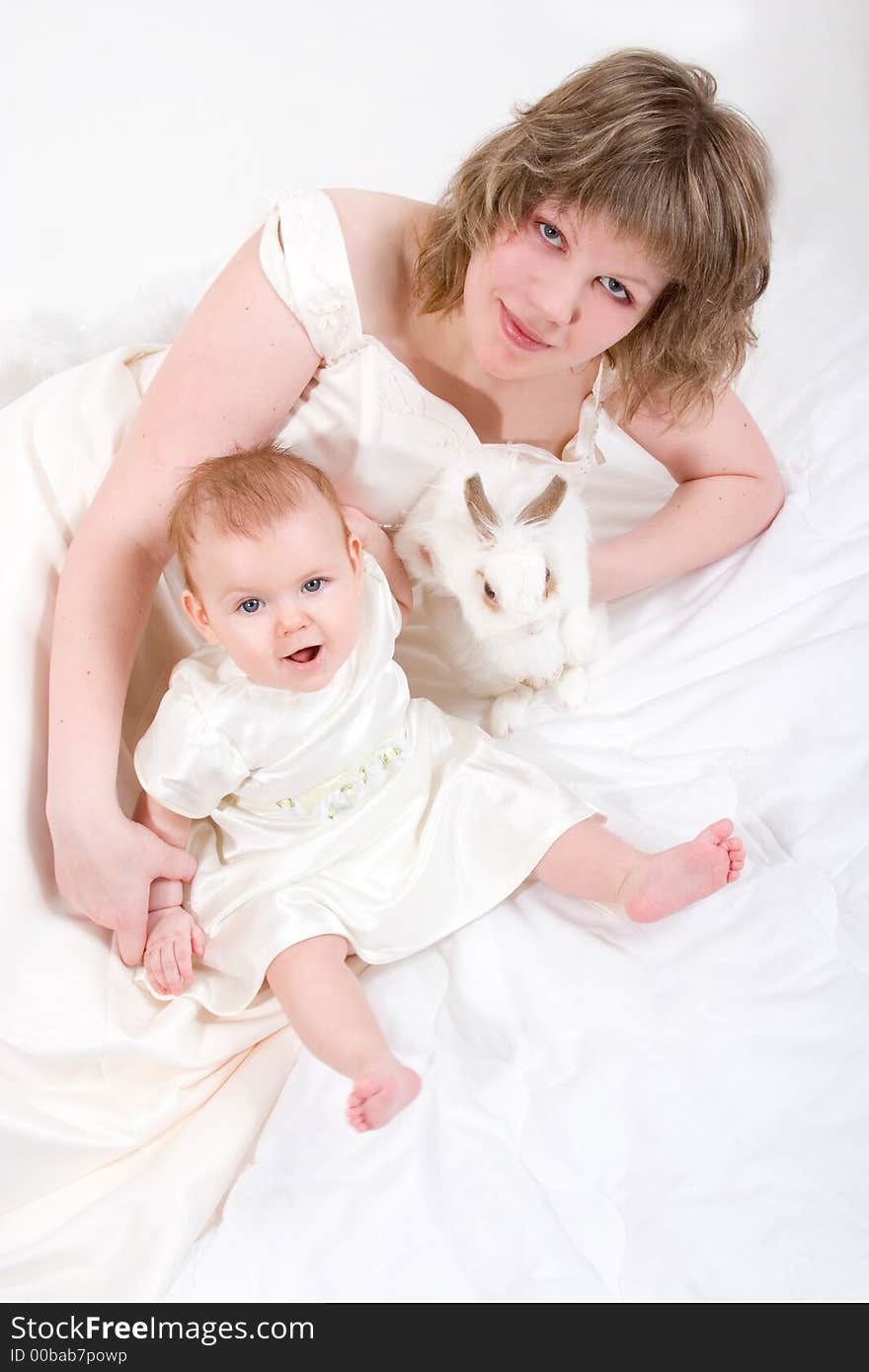 Mother and baby with rabbit are posing on white and looking into the camera