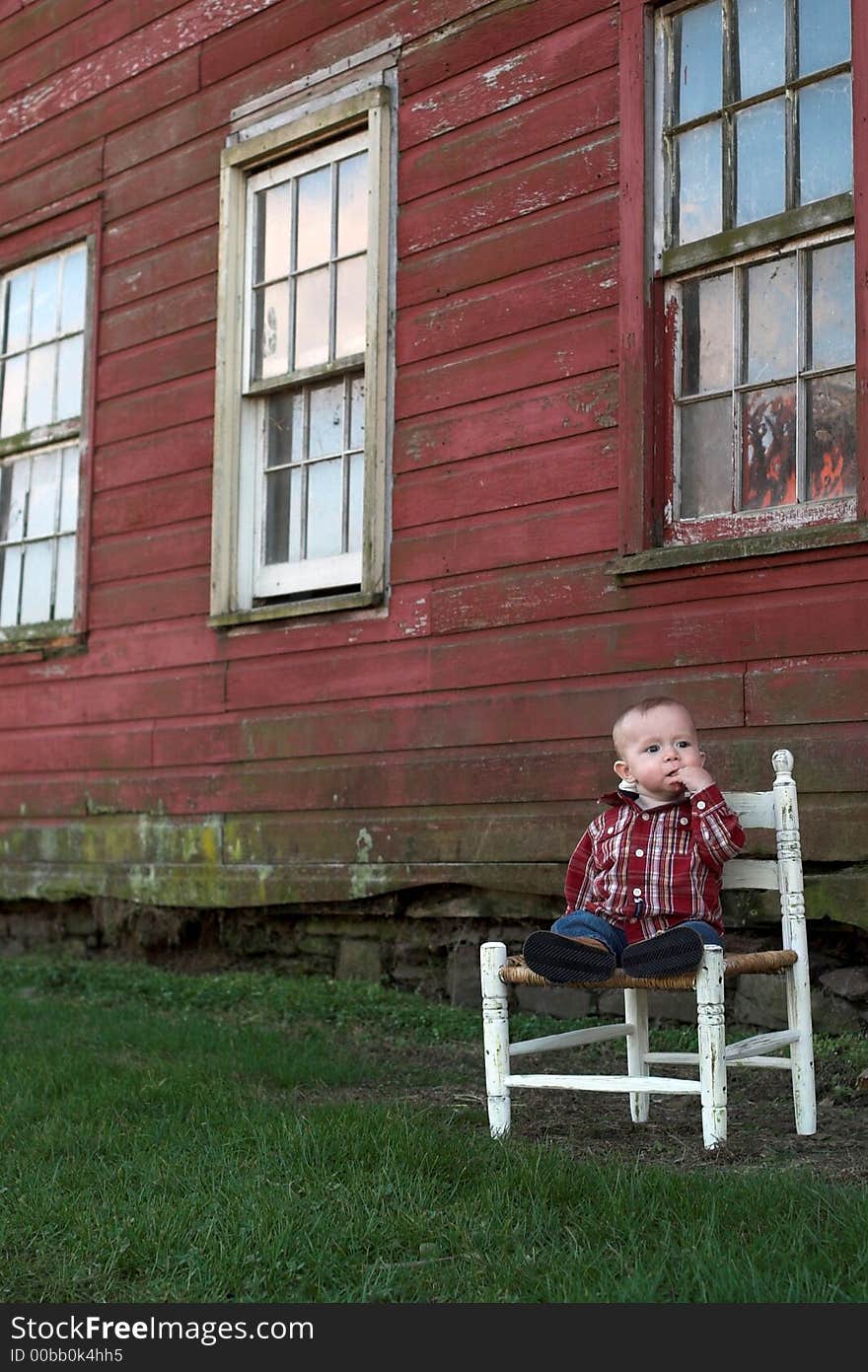 Image of baby boy sitting on a chair in front of a red farm building. Image of baby boy sitting on a chair in front of a red farm building