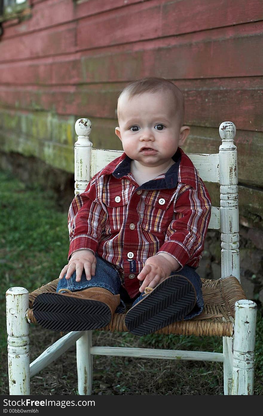 Image of baby boy sitting on a chair in front of a red farm building. Image of baby boy sitting on a chair in front of a red farm building