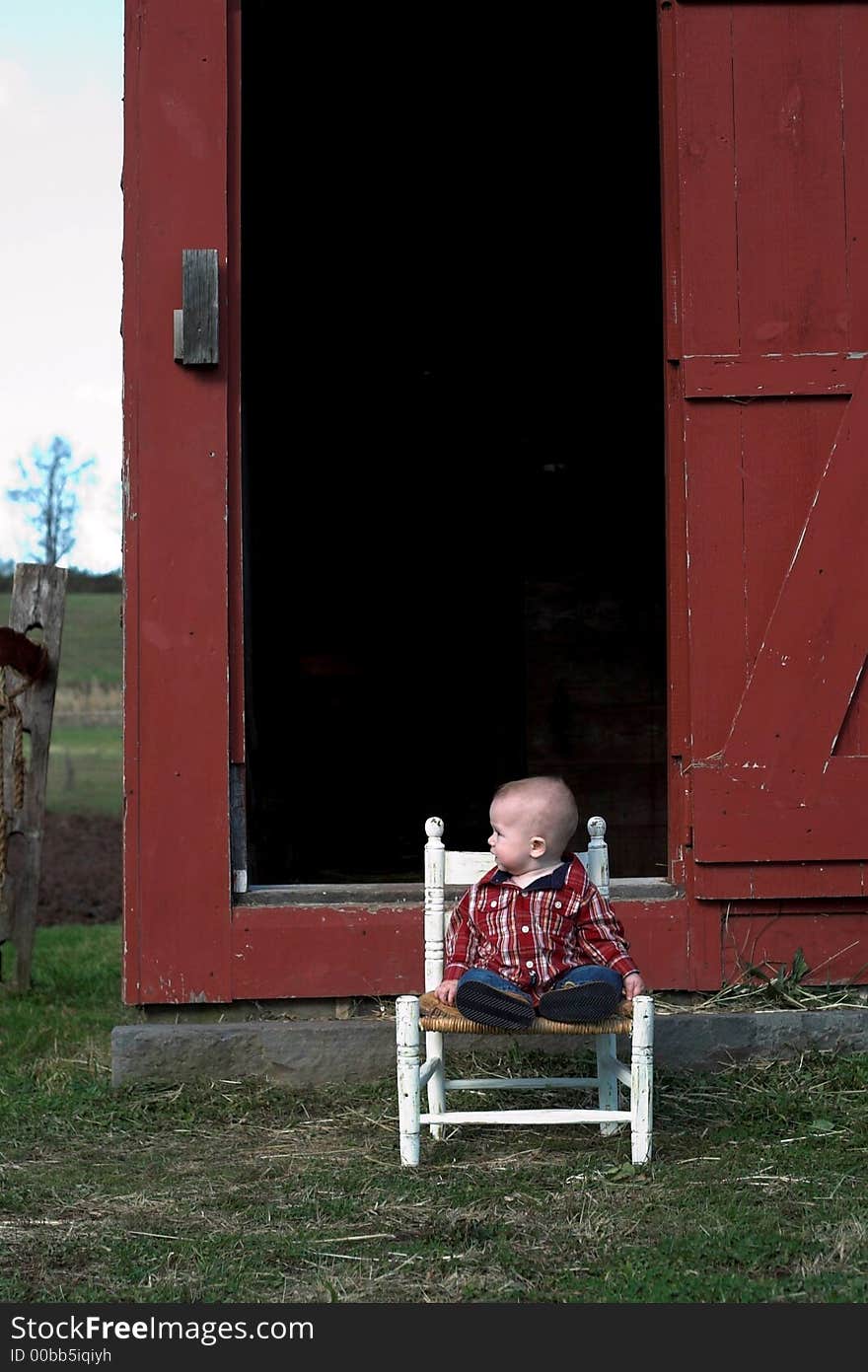 Image of baby boy sitting on a chair in front of a red farm building. Image of baby boy sitting on a chair in front of a red farm building