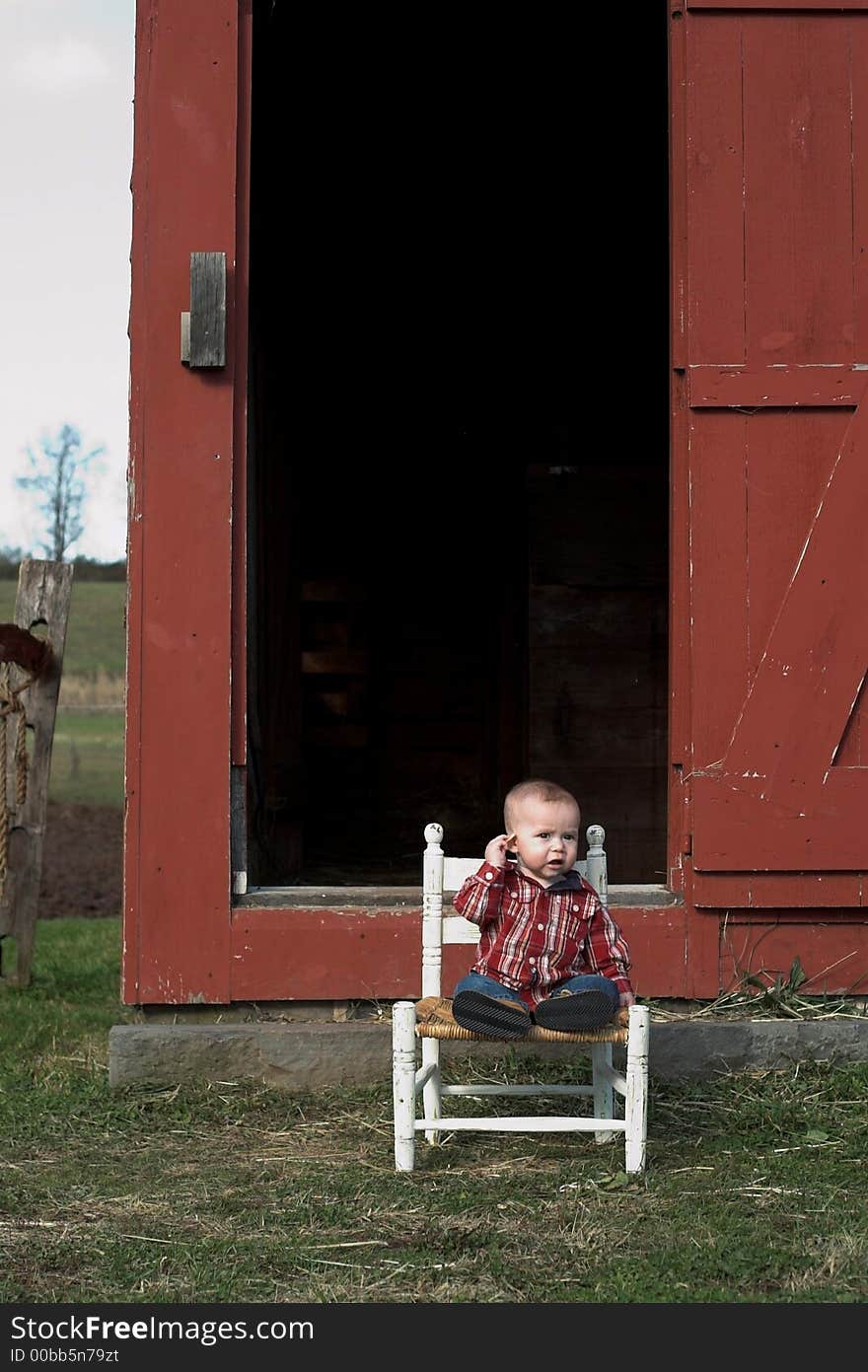 Image of baby boy sitting on a chair in front of a red farm building. Image of baby boy sitting on a chair in front of a red farm building