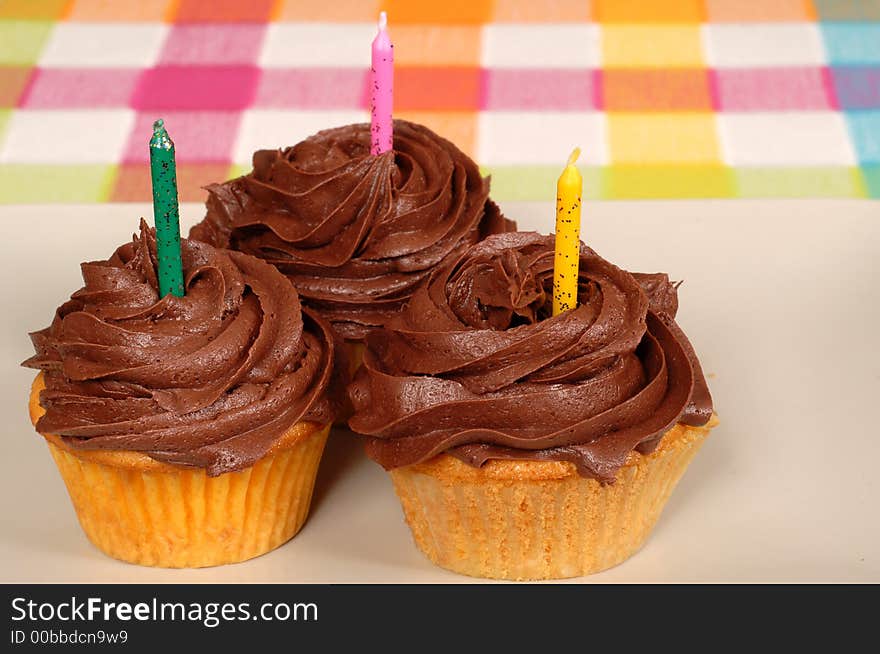 Three chocolate frosted cupcakes with candles