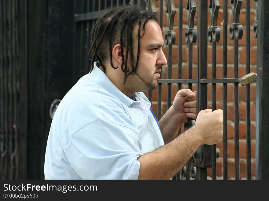 Photo of a young man standing on the sidewalk grasping a gate enterance. Photo of a young man standing on the sidewalk grasping a gate enterance