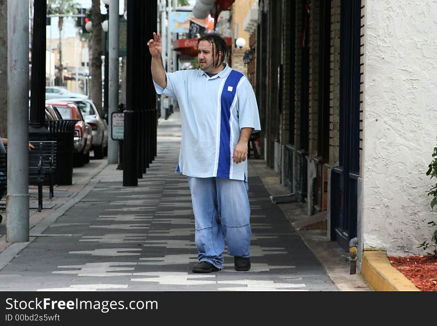 Photo of a young man walking down the sidewalk, waving to a friend. Photo of a young man walking down the sidewalk, waving to a friend